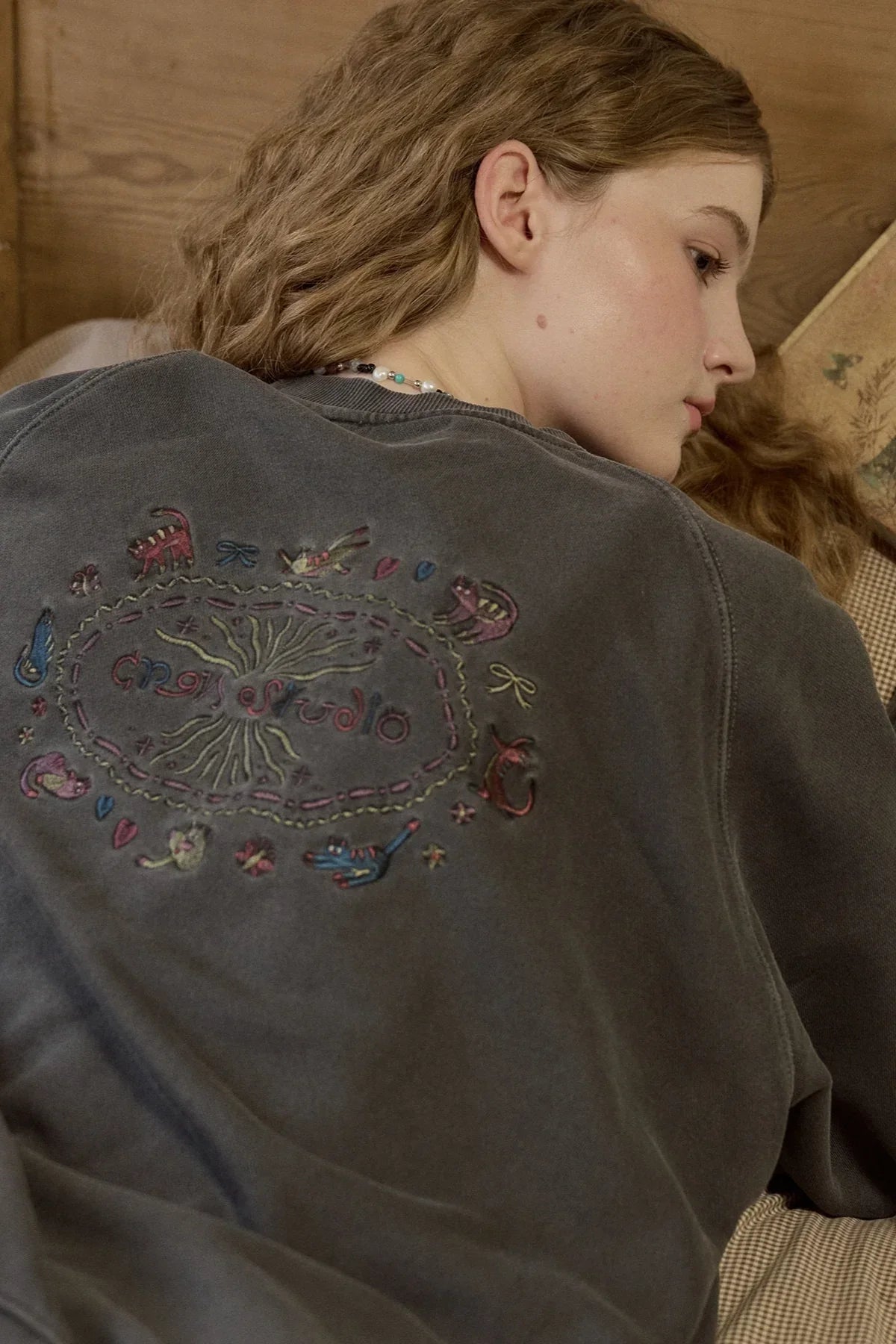 Close-up of woman wearing dark smoke black raglan sweatshirt with colorful embroidered cat and text design on back