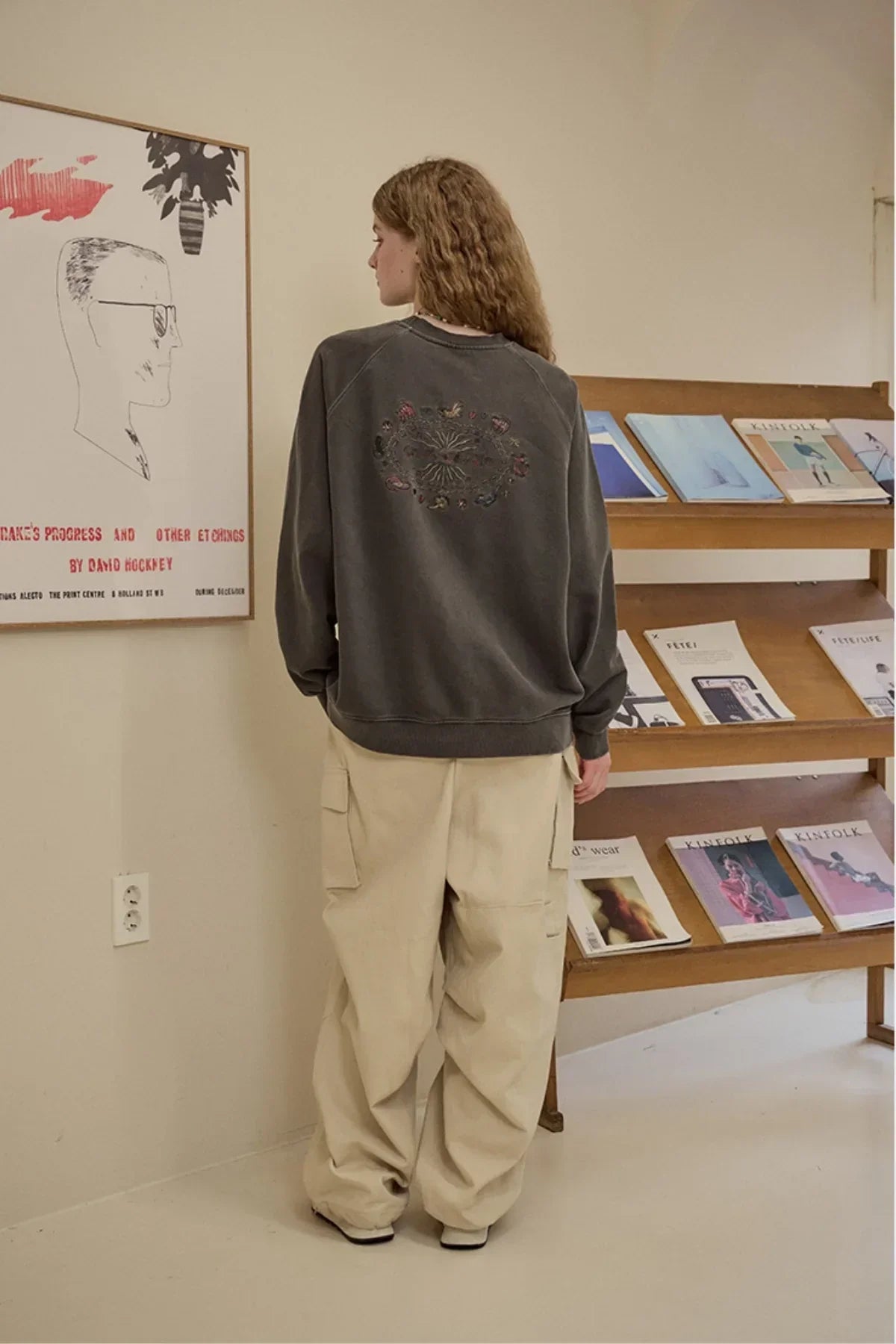 Woman in oversized black sweatshirt with embroidered back design and beige cargo pants in minimalist room