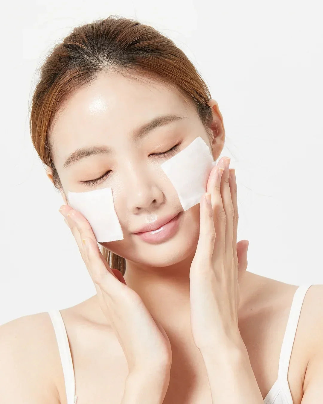 Woman with closed eyes applying cotton pads on cheeks for skincare, glowing clear skin