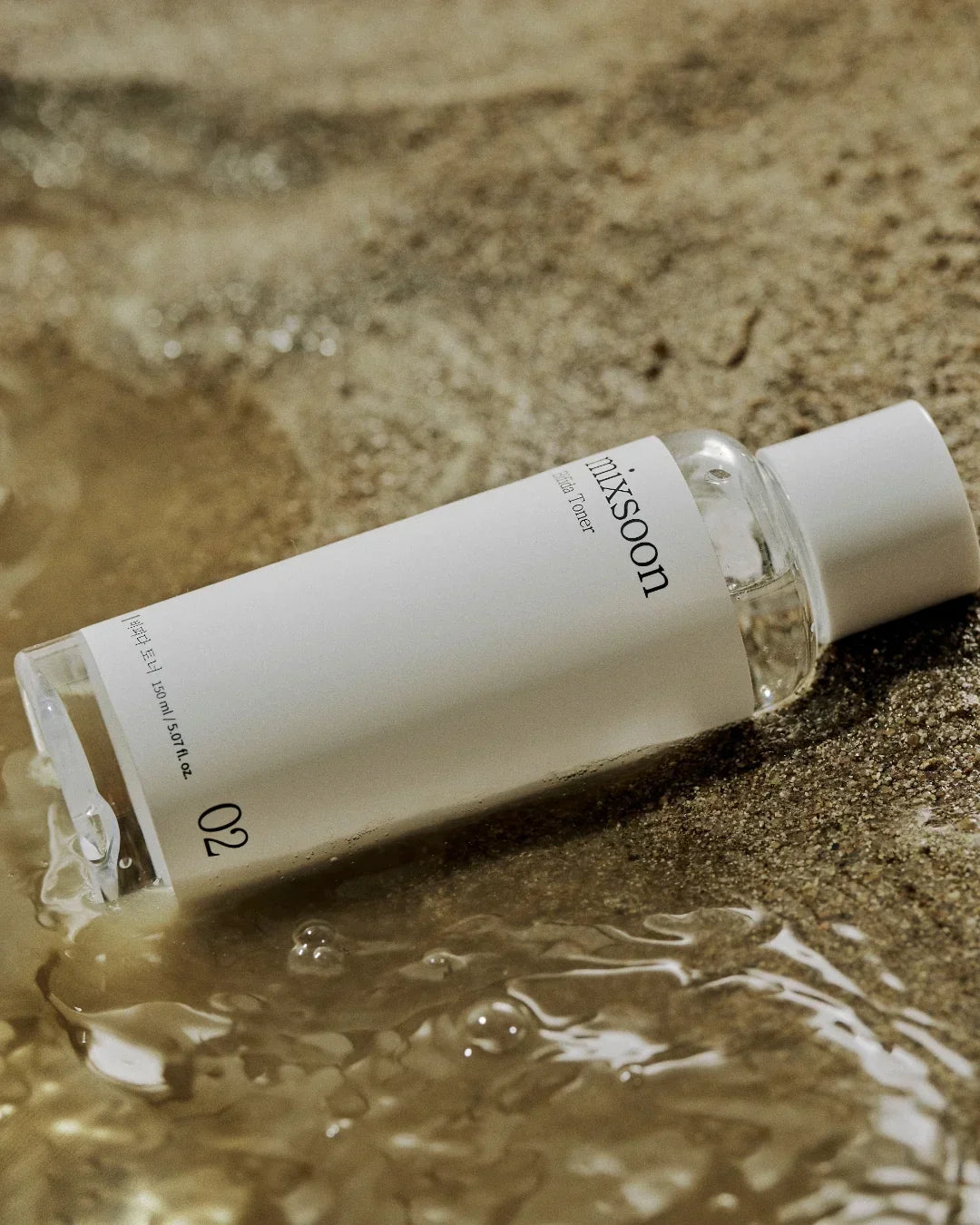 Mixsoon Centella Asiatica Toner 150ml bottle lying on wet sandy surface with water