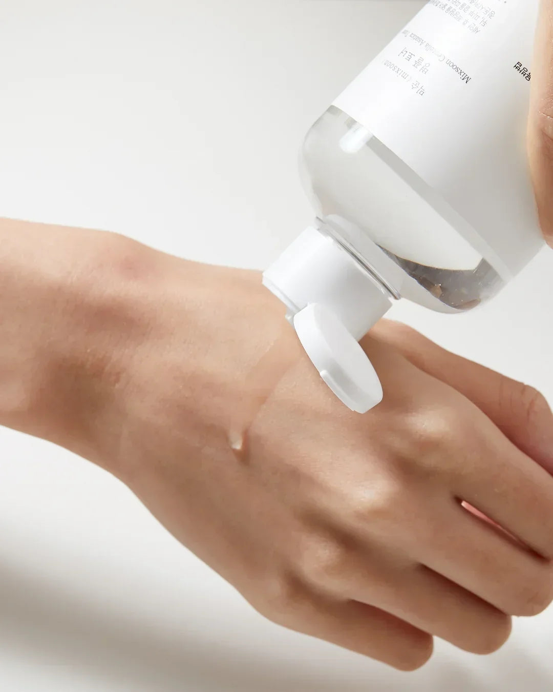 Clear toner liquid being dispensed onto hand from white-capped transparent bottle in skincare demonstration