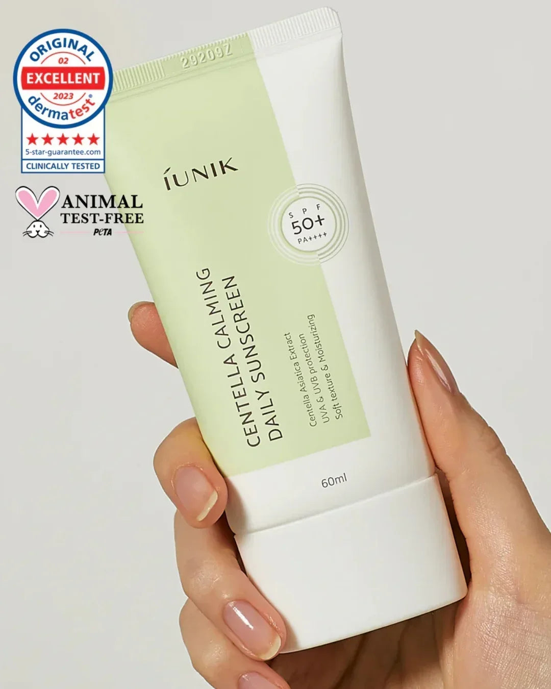 Hand holding iUNIK Centella Calming Daily Sunscreen SPF 50+ PA++++ tube with animal test-free and dermatologist tested labels