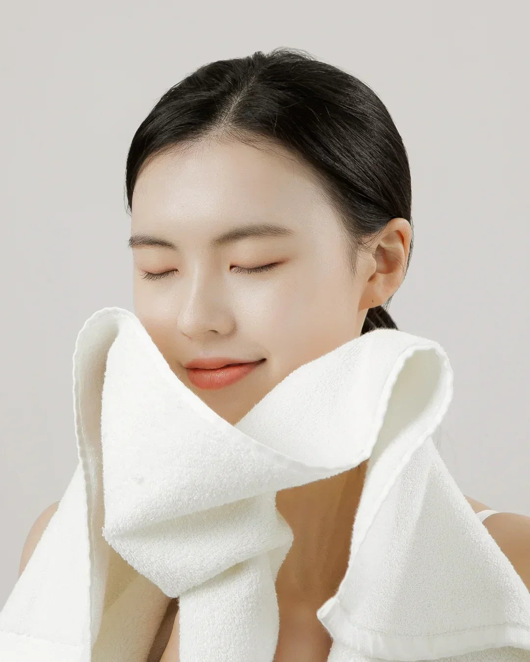 Young woman with smooth skin gently holding a soft white towel to her face