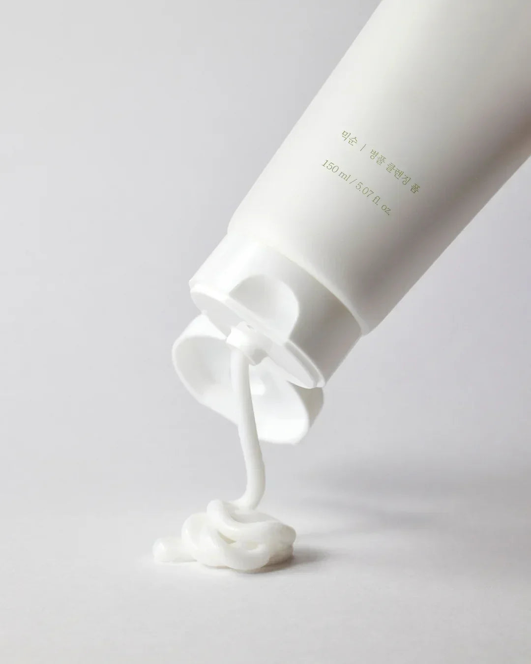 White tube dispenser pouring white Centella cleansing foam cream on a light surface