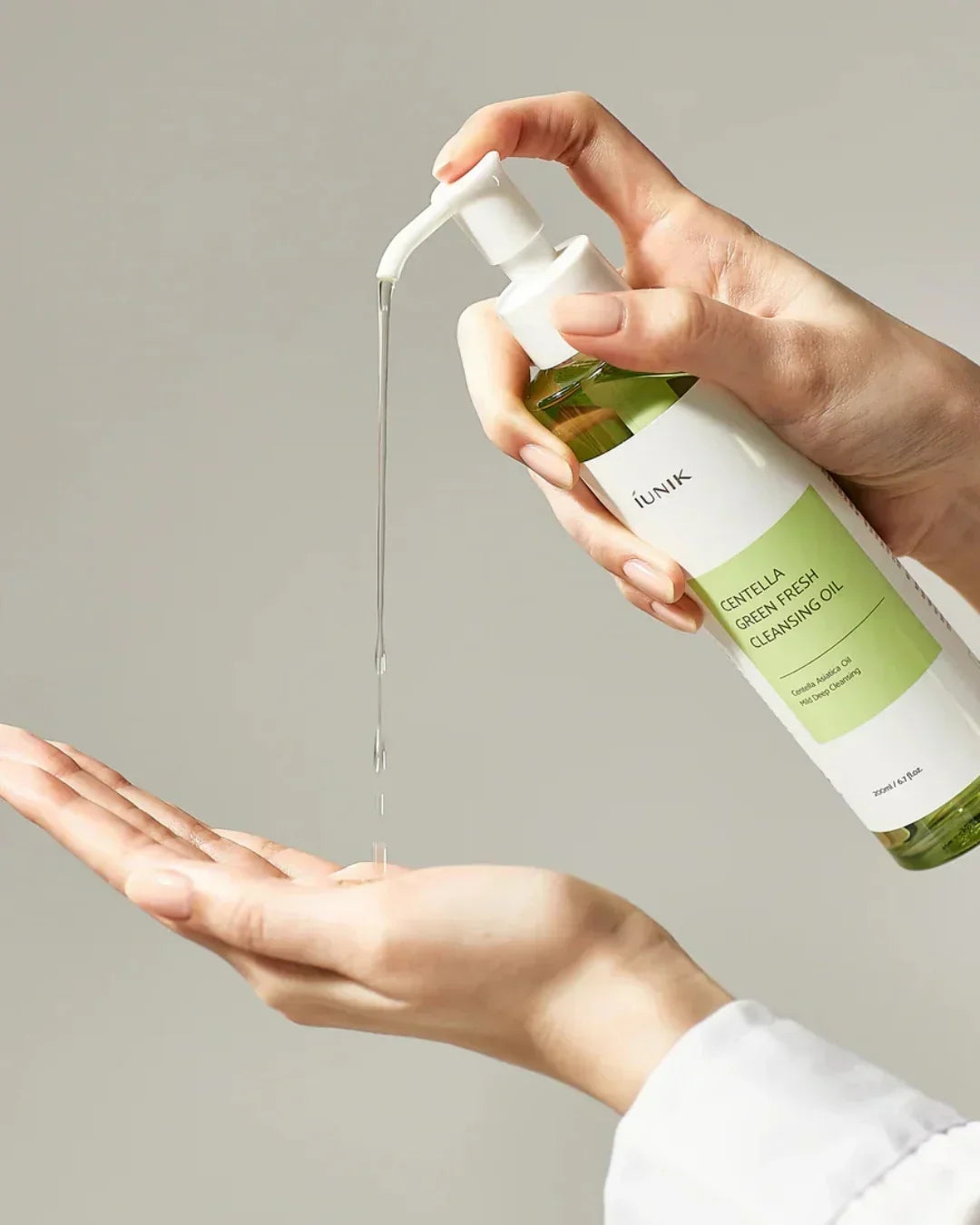 Person dispensing IUNIK Centella Green Fresh Cleansing Oil into hand with gray background