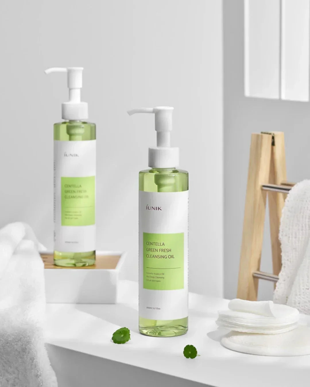 iUNIK Centella Green Fresh Cleansing Oil bottles with cotton pads and towel in bright bathroom setting