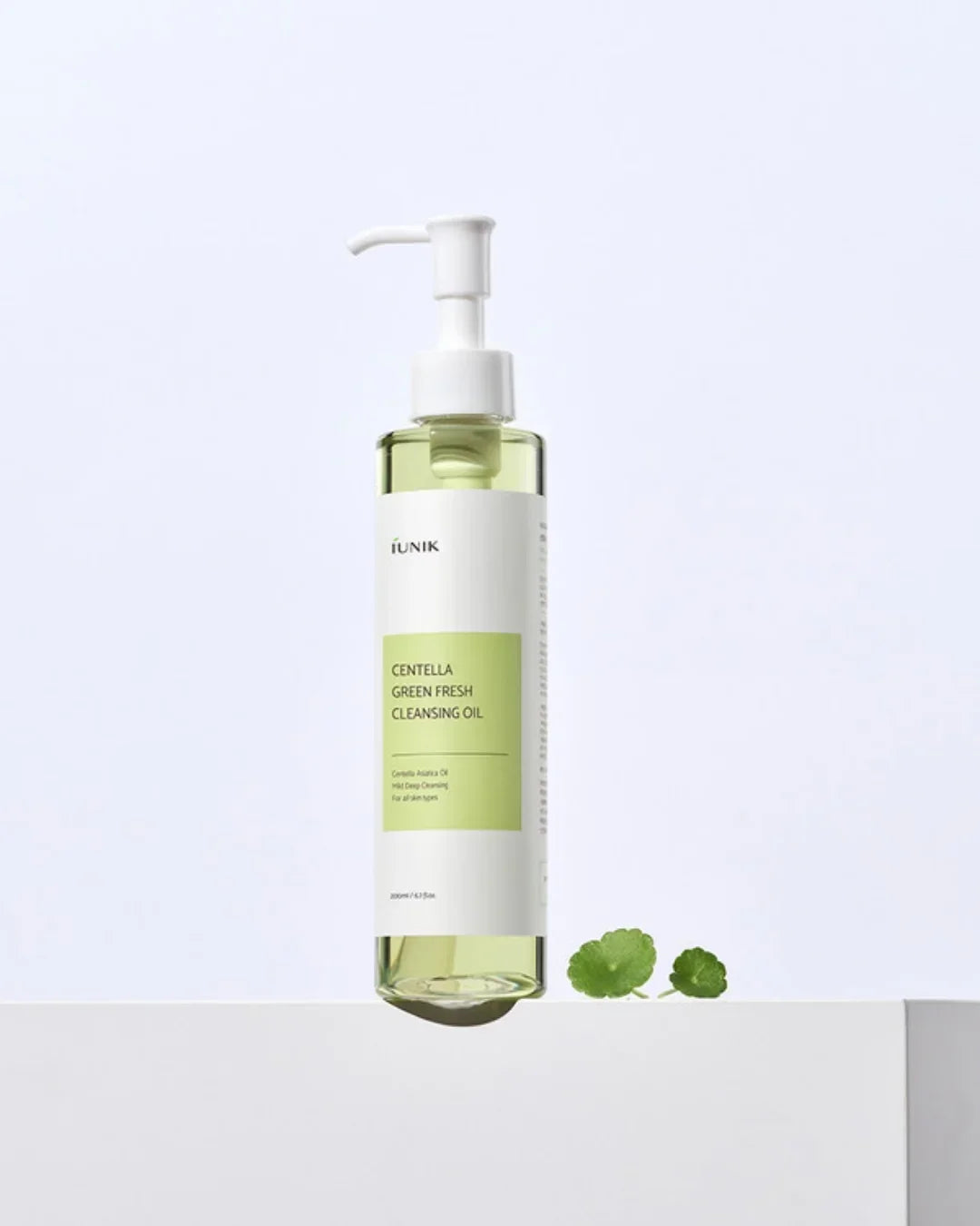 iUNIK Centella Green Fresh Cleansing Oil bottle with pump on white surface and small green leaves