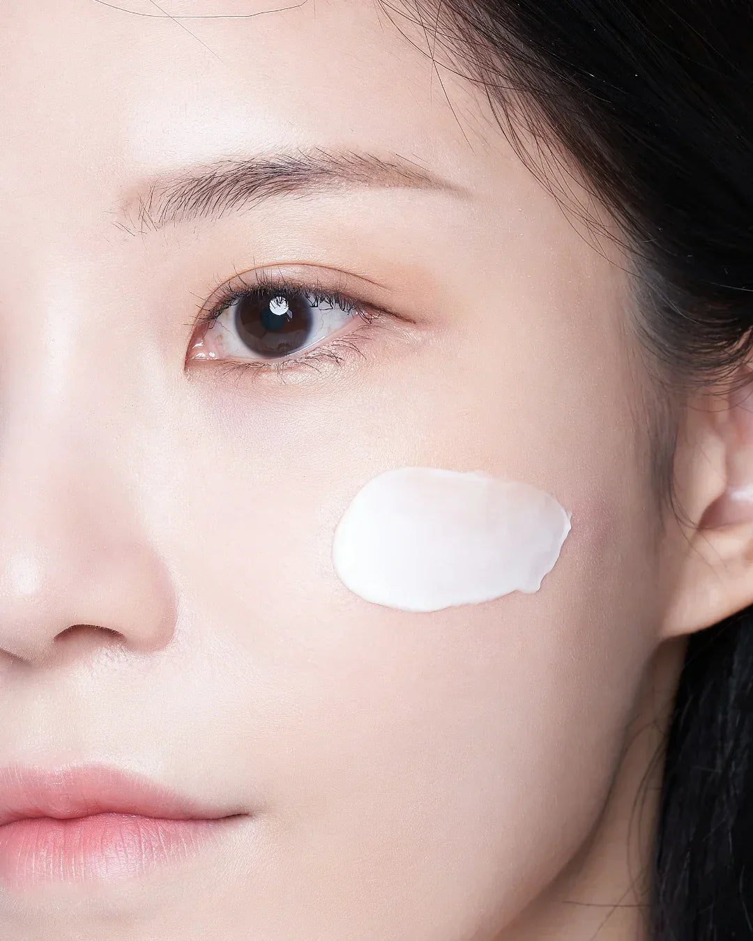 Close-up of woman's face with smooth skin and white cream applied on cheek for skincare