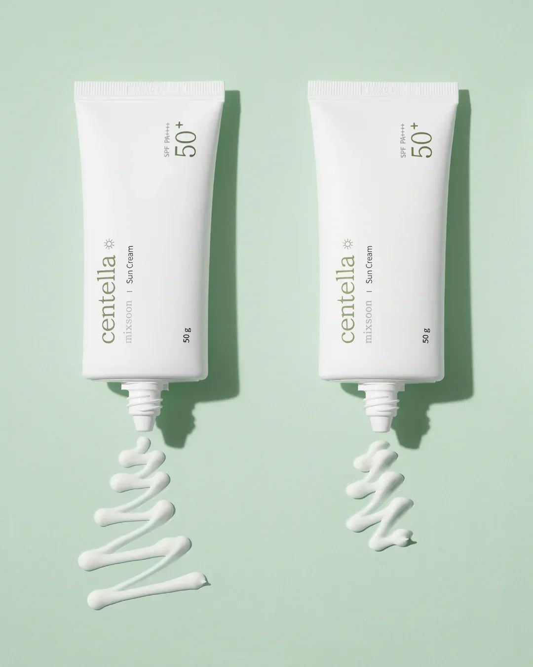 Two tubes of Centella Mixsoon Sun Cream SPF 50+ with white cream swirls on pastel green background