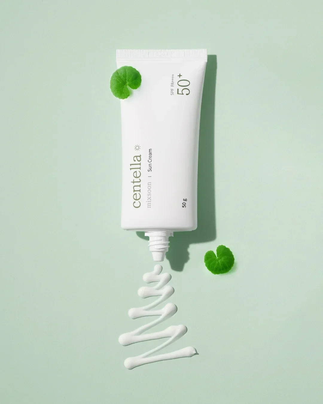 Tube of Centella SPF 50+ sun cream with cream swirled on light green background and centella leaves