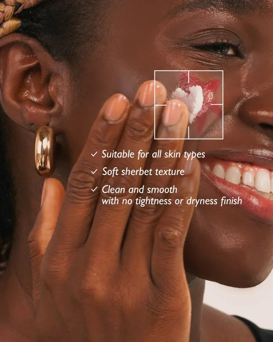 Close-up of smiling woman applying white sherbet texture cleansing balm over red makeup on cheek, demonstrating gentle makeup removal
