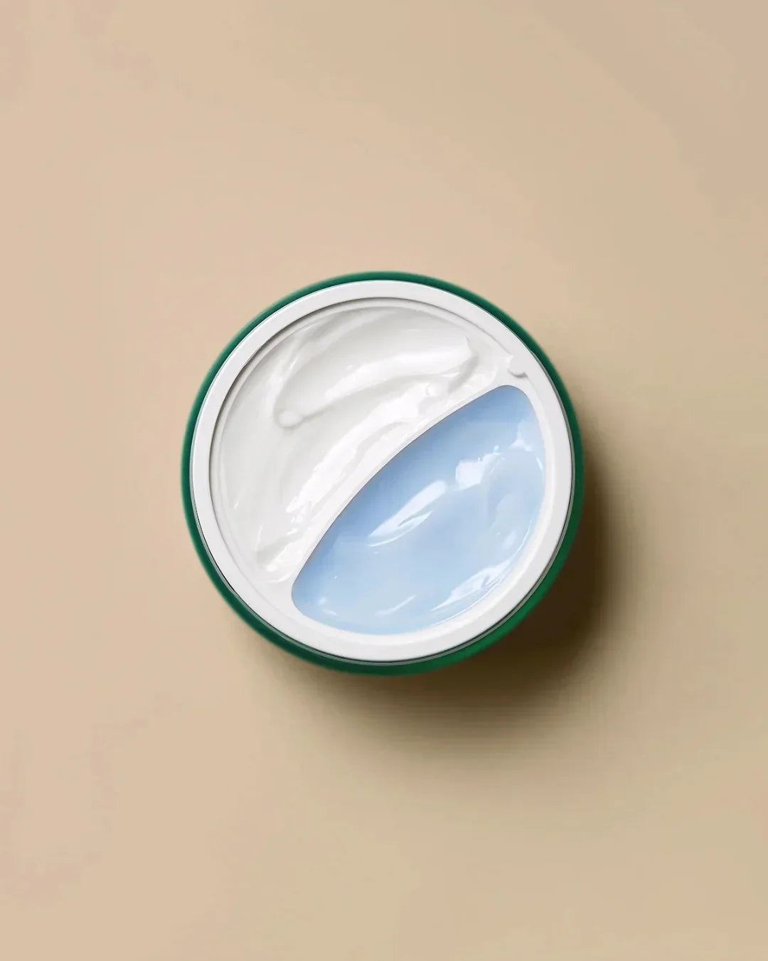 Open cream jar with separated white and light blue moisturizing creams on beige background