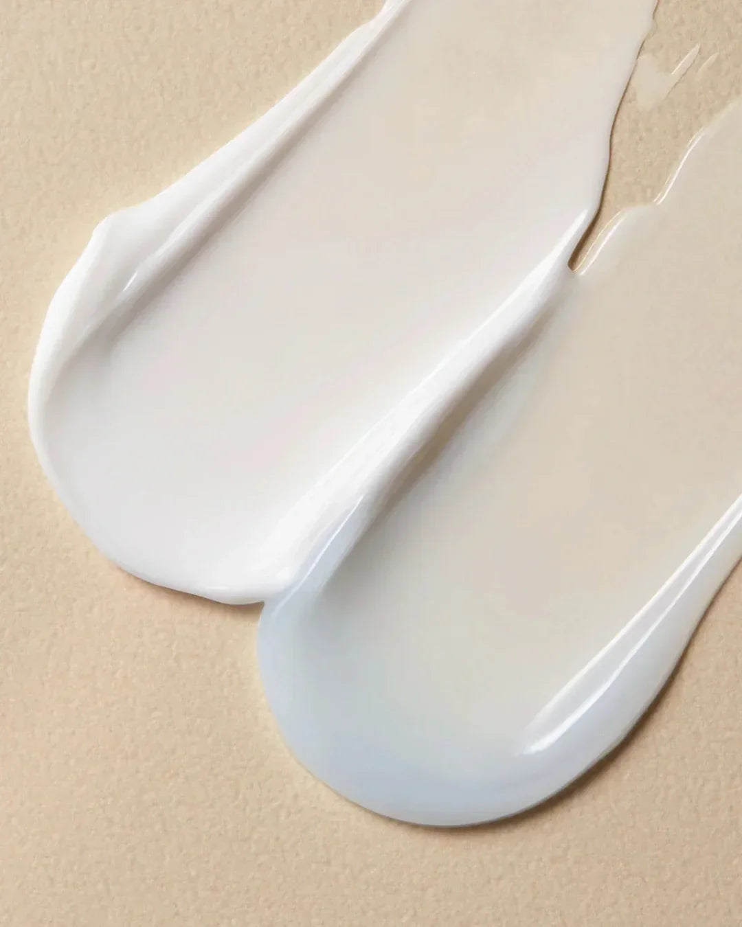 Close-up of two creamy cosmetic lotion textures on a beige surface