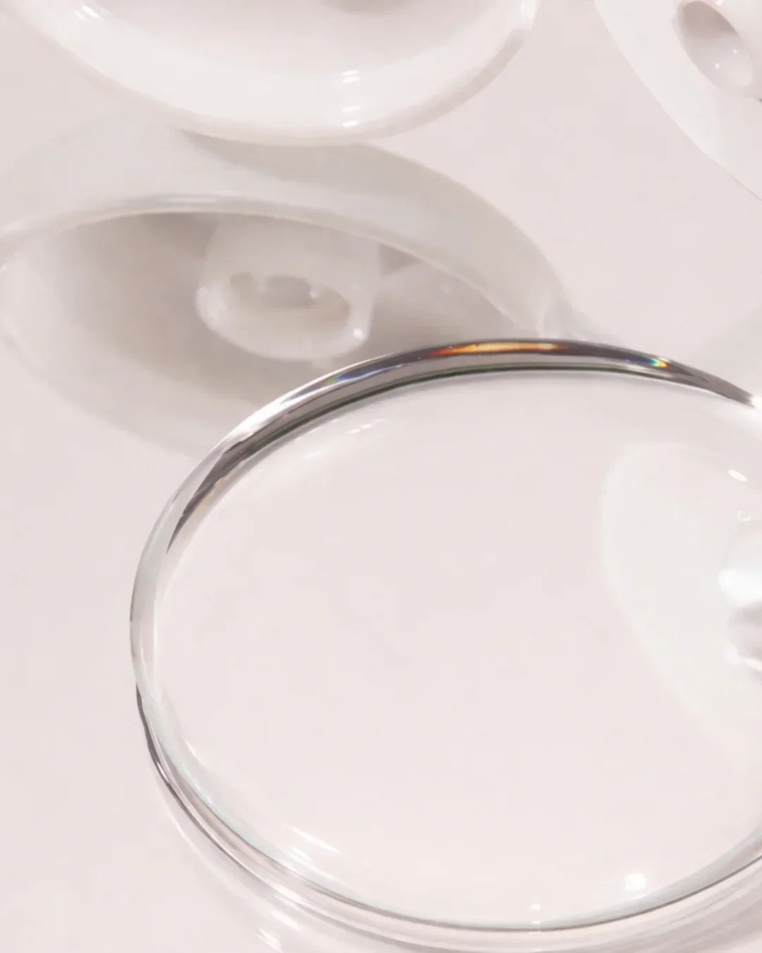 Close-up of clear liquid texture inside transparent cosmetic containers on white surface