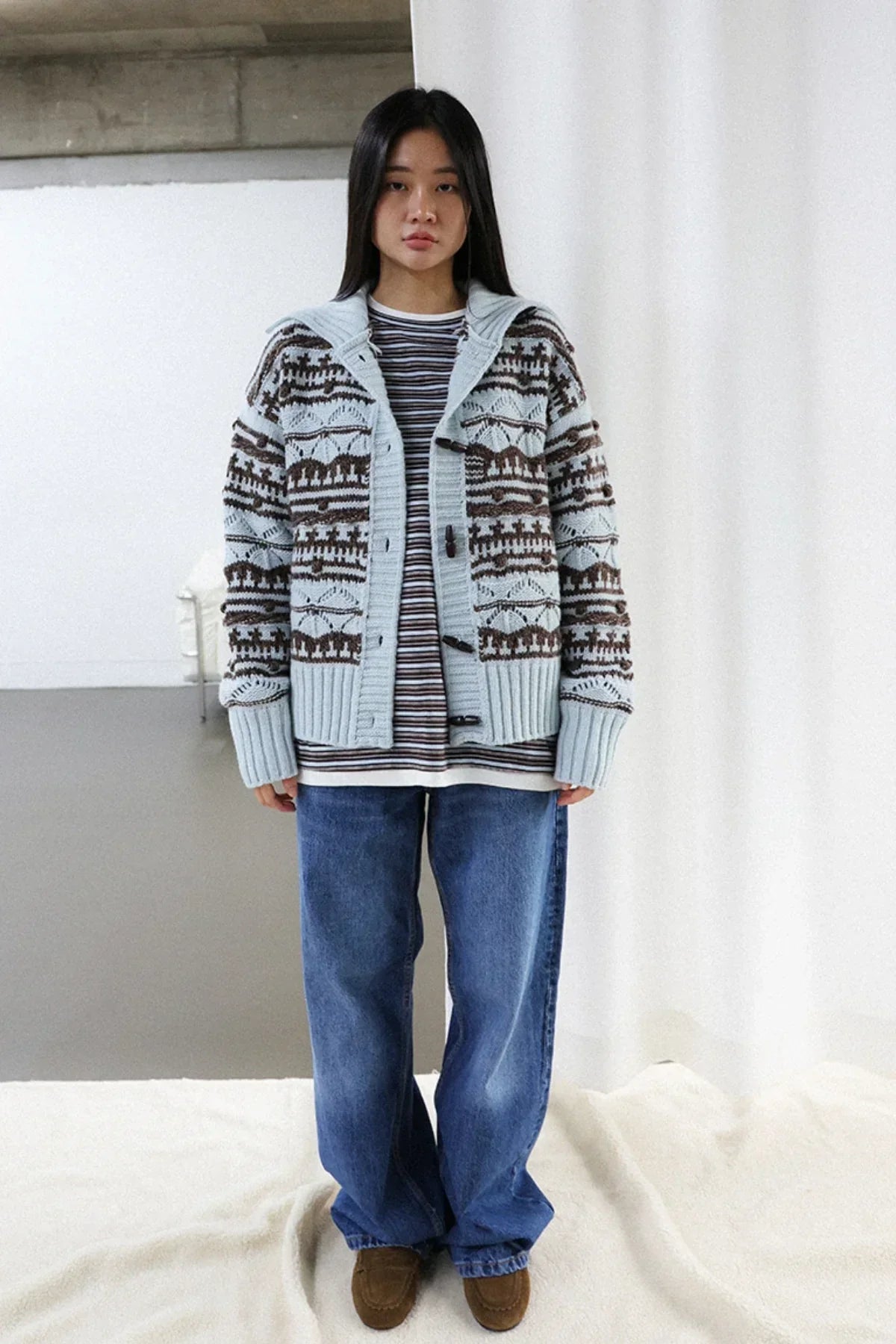 Woman wearing chunky collar box fit cardigan in mint and chocolate with striped shirt, blue jeans, and brown shoes