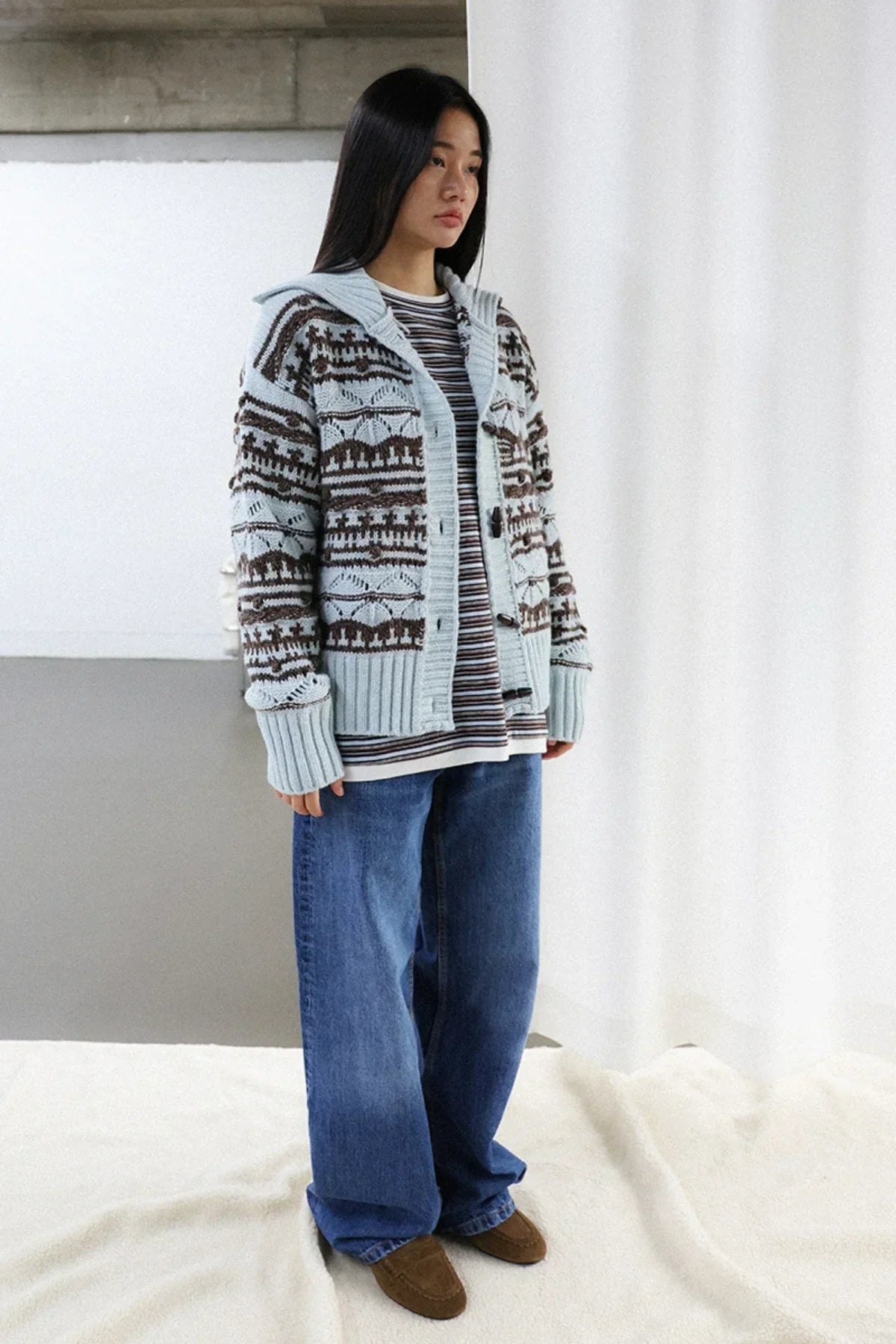Woman wearing a chunky collar knit cardigan with pattern, striped shirt, loose blue jeans, and brown shoes