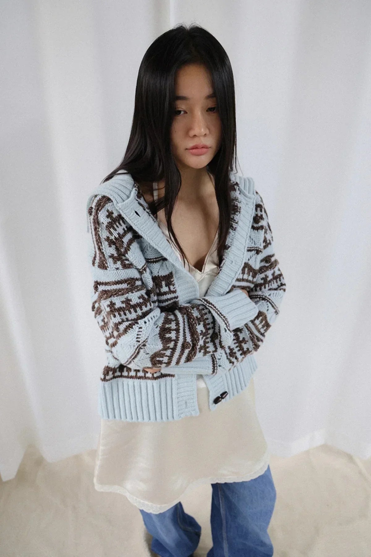 young woman wearing chunky knit cardigan with blue and brown pattern over slip dress and jeans