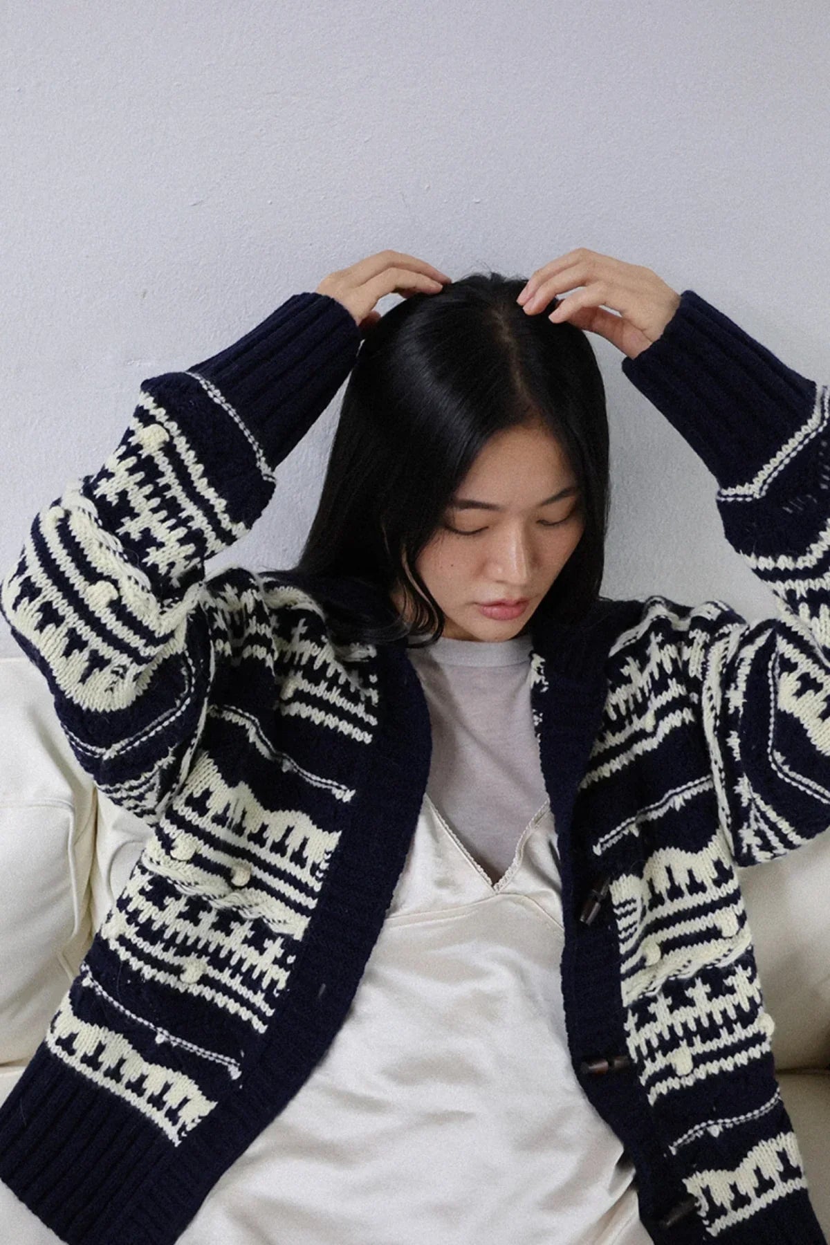 Woman wearing navy chunky collar box-fit cardigan with cream patterns sitting on white sofa