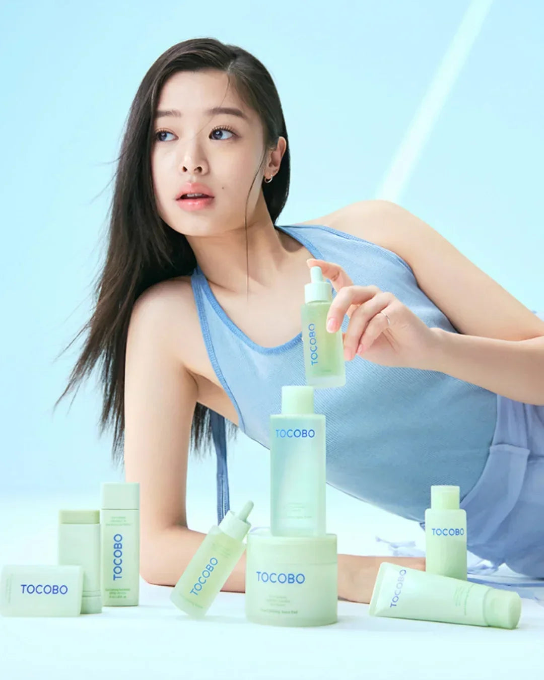 Young woman in blue top posing with TOCOBO skincare products on light blue background