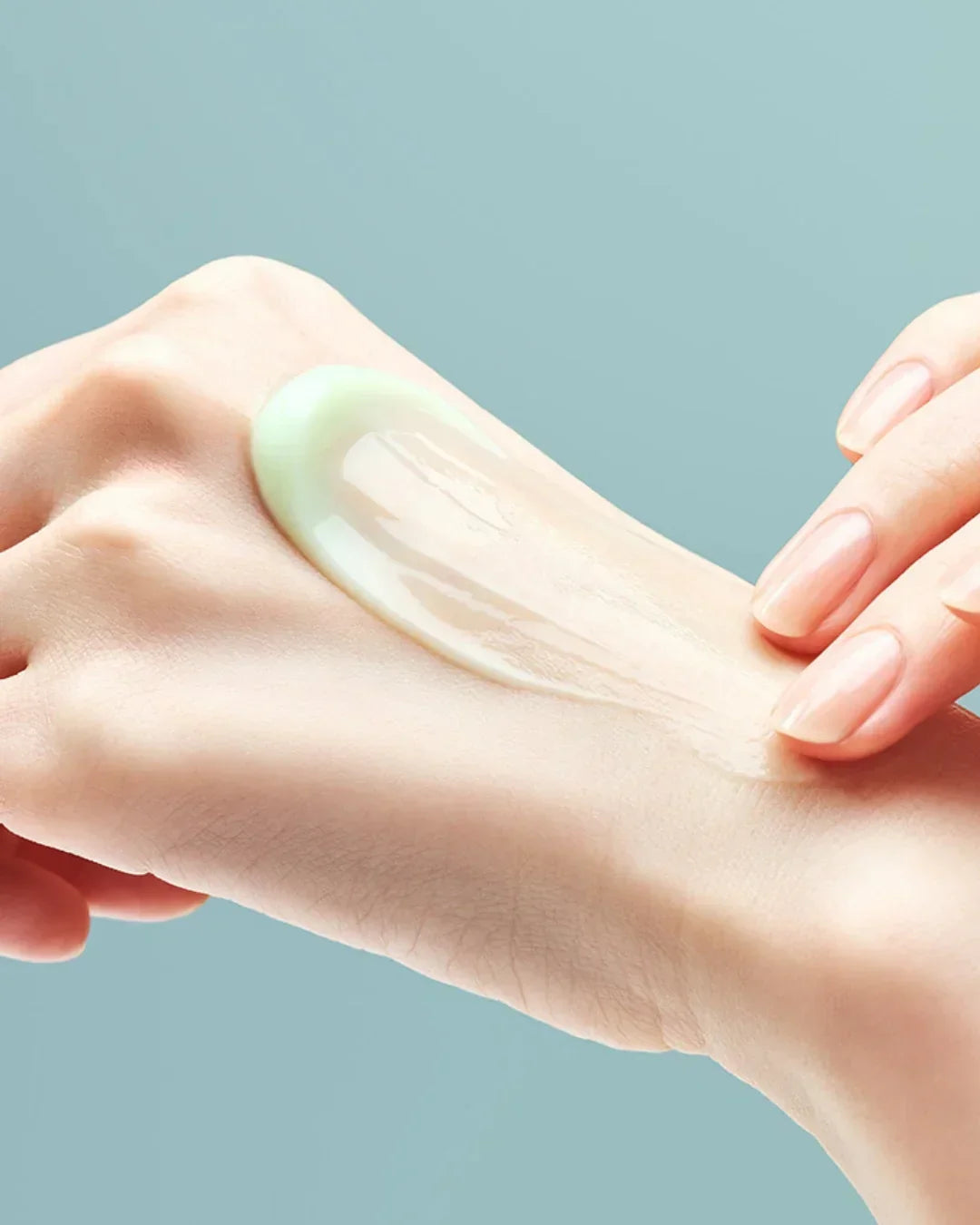 Hand applying smooth light green gel cream on skin with blue background
