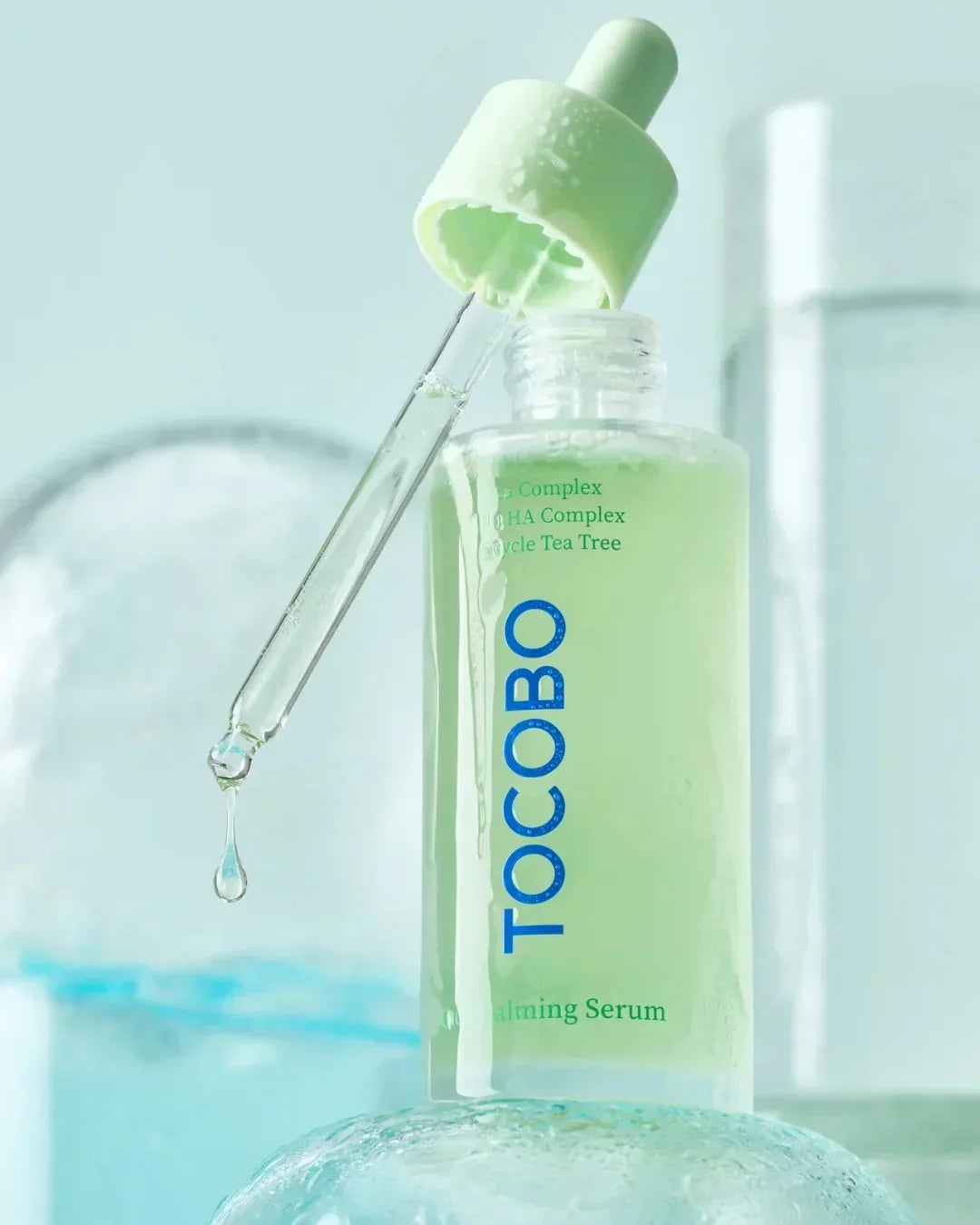 Tocobo green calming serum bottle with dropper releasing liquid drop in a light blue setting