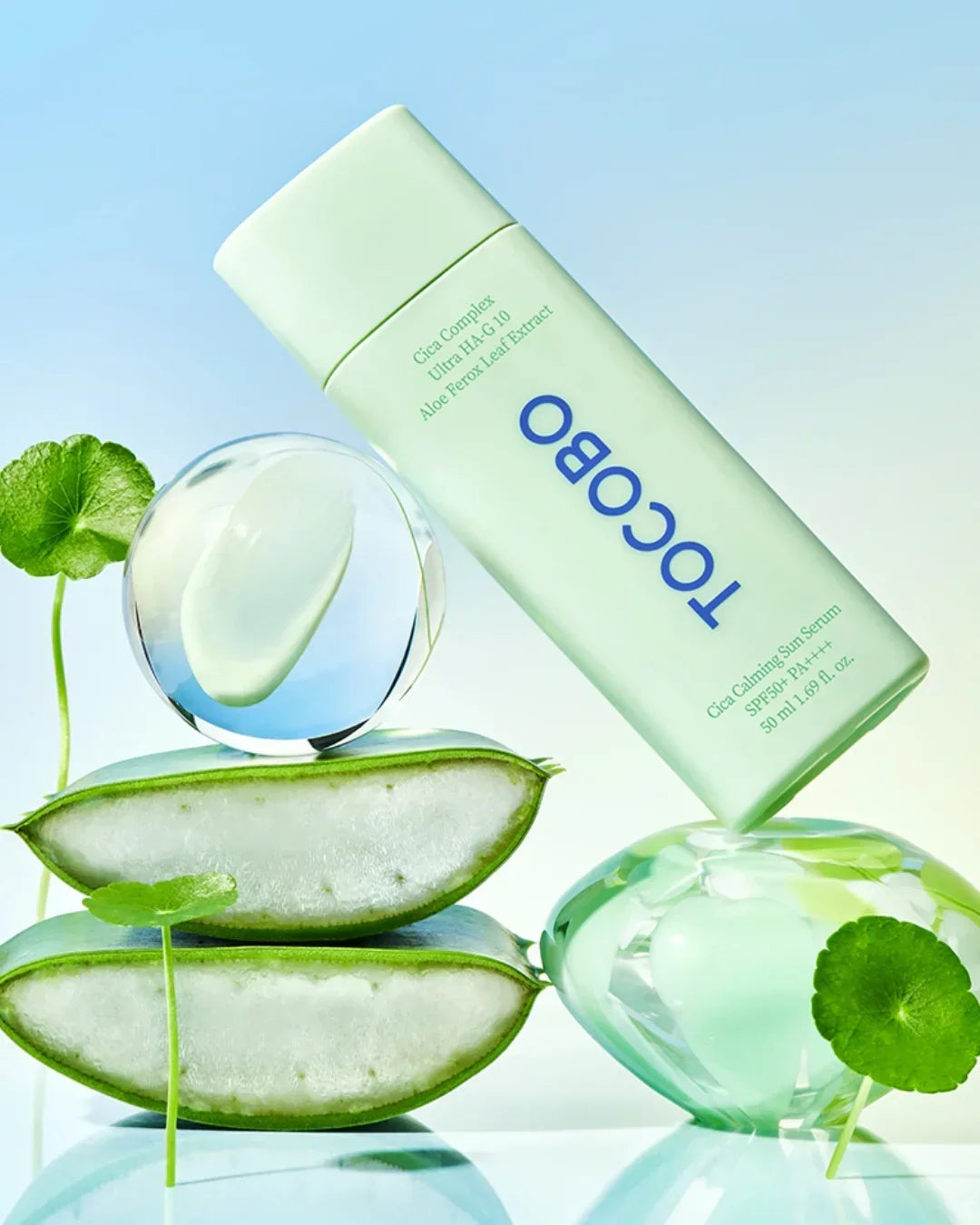 Tocobo Cica Calming Sun Serum bottle with aloe and green leaves on reflective surface