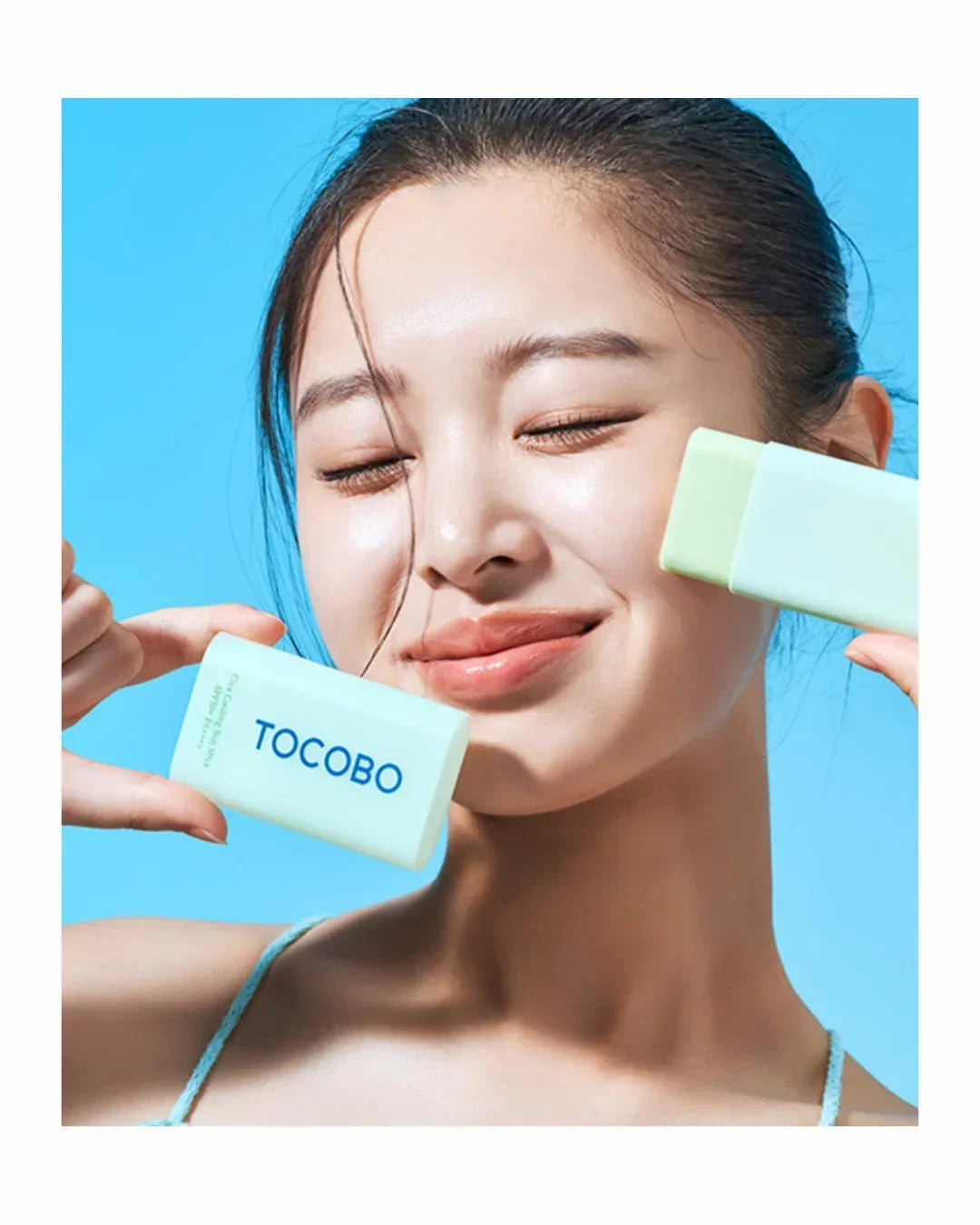Smiling woman holding Tocobo green cooling sun stick SPF50 PA against blue background