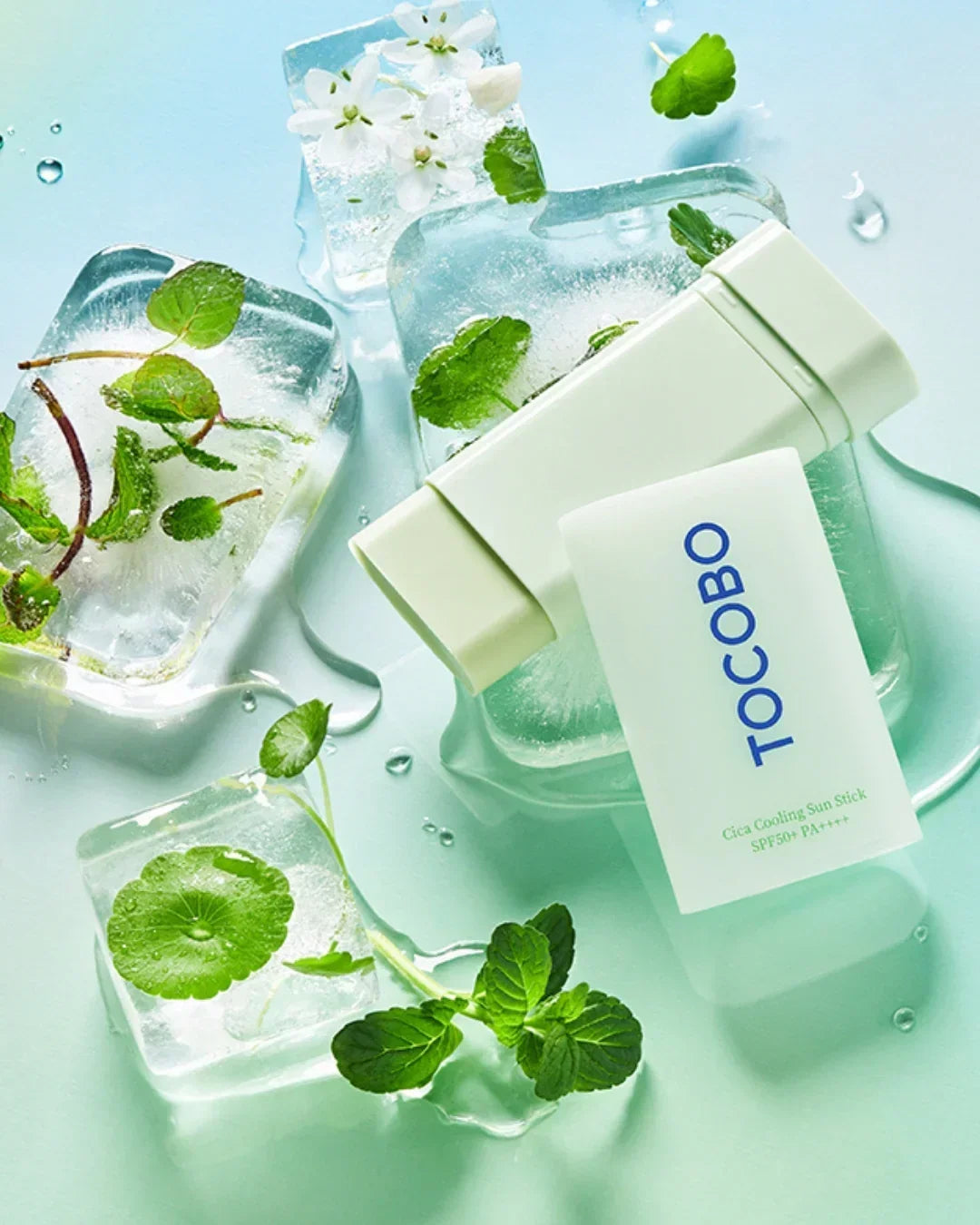 TOCOBO Cica Cooling Sun Stick SPF50 PA++++ with ice cubes and green leaves on light blue surface