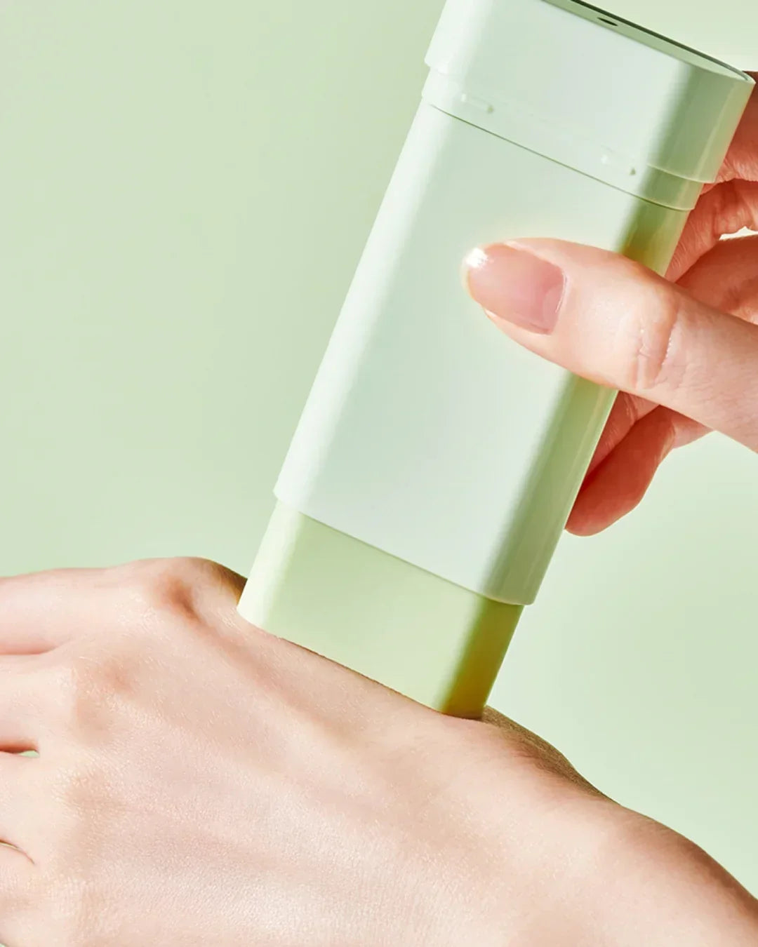 Hand applying green cooling sun stick with SPF 50 PA on skin against light green background