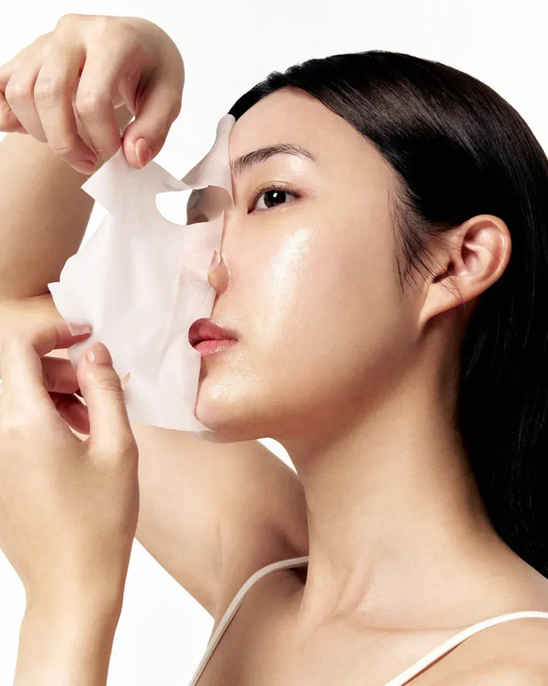 Close-up of woman peeling off a white sheet face mask, showcasing clear glowing skin