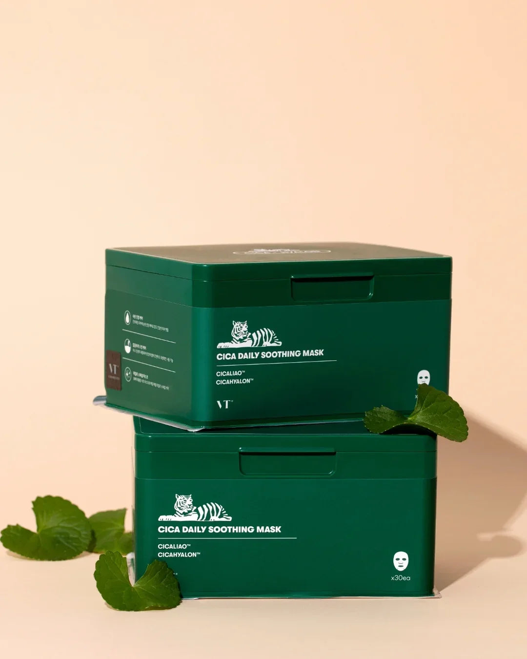 Two green VT Cica Daily Soothing Mask boxes stacked with centella leaves on beige background