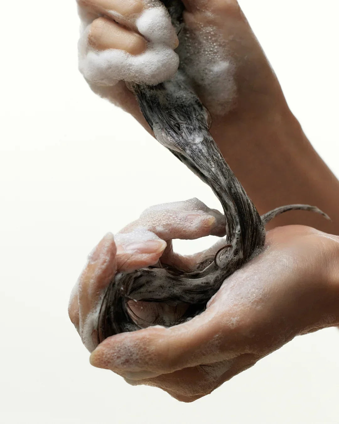 Foamy black hair being washed with shampoo, hands massaging scalp and strands