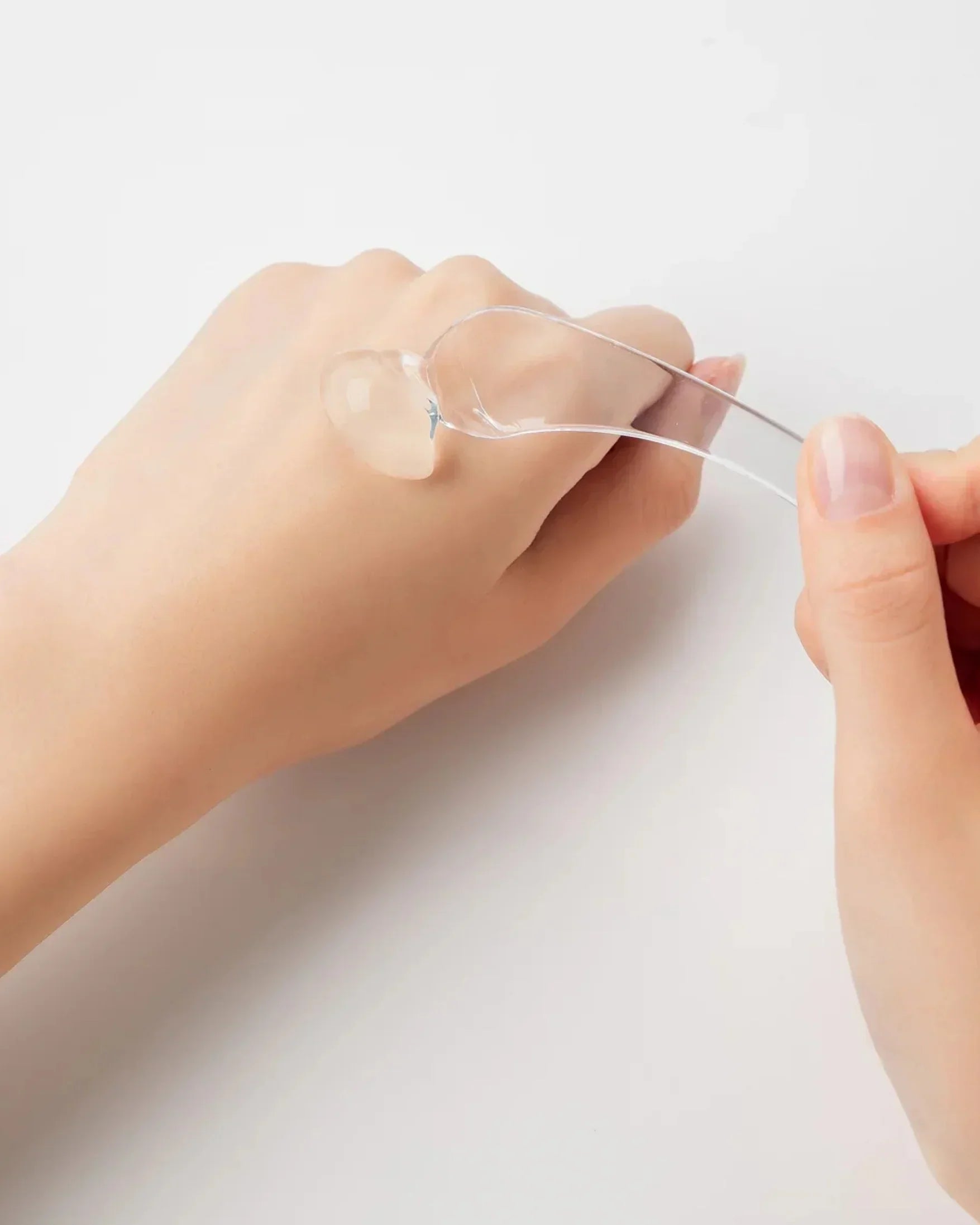 Hand holding clear spatula applying transparent soothing gel on the back of another hand