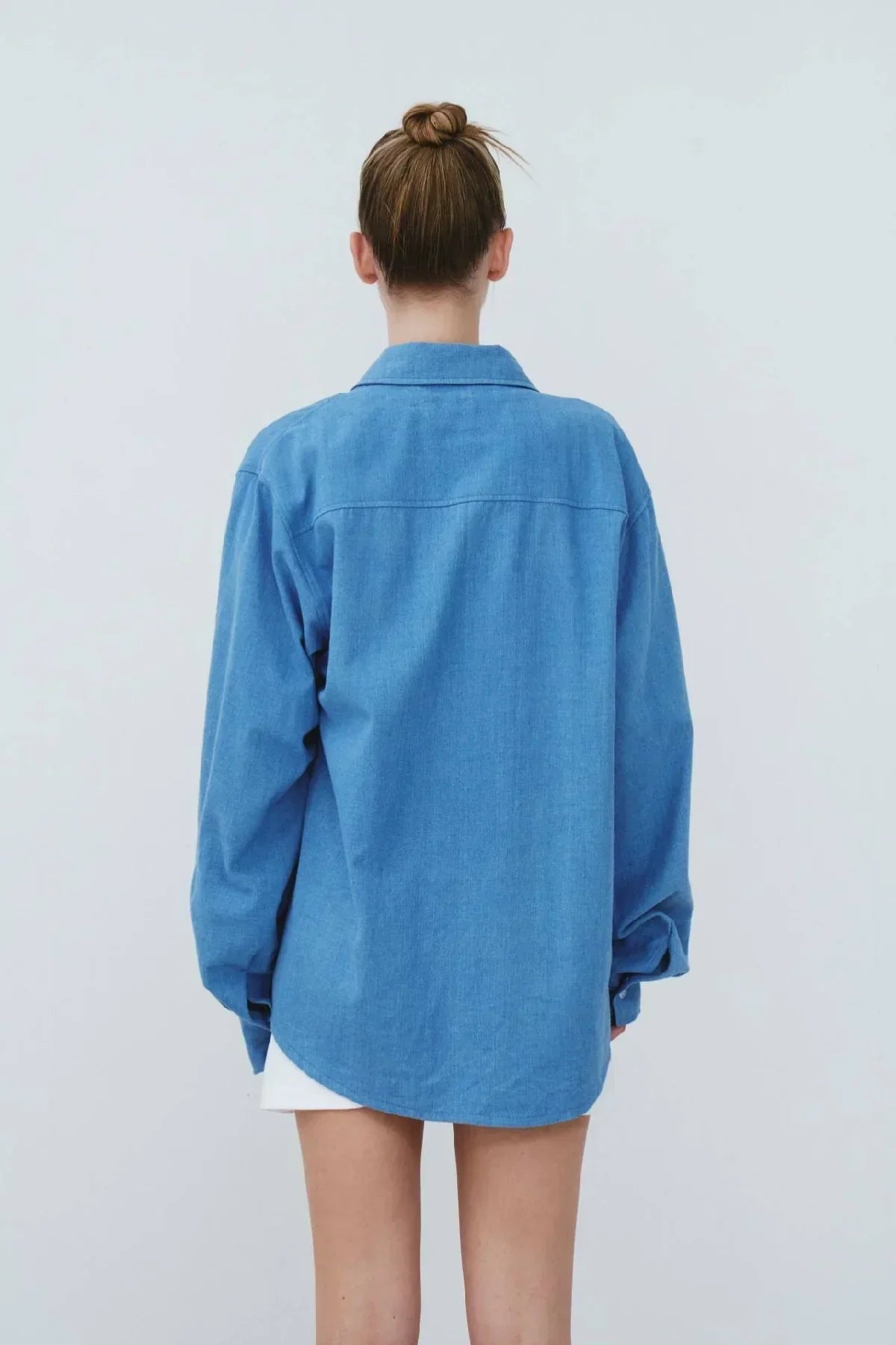 Back view of person wearing oversized light blue denim shirt with long sleeves and collar