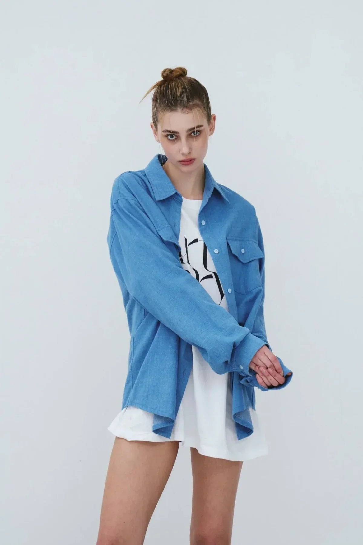 Young woman wearing light blue oversized denim shirt over white graphic tee in studio