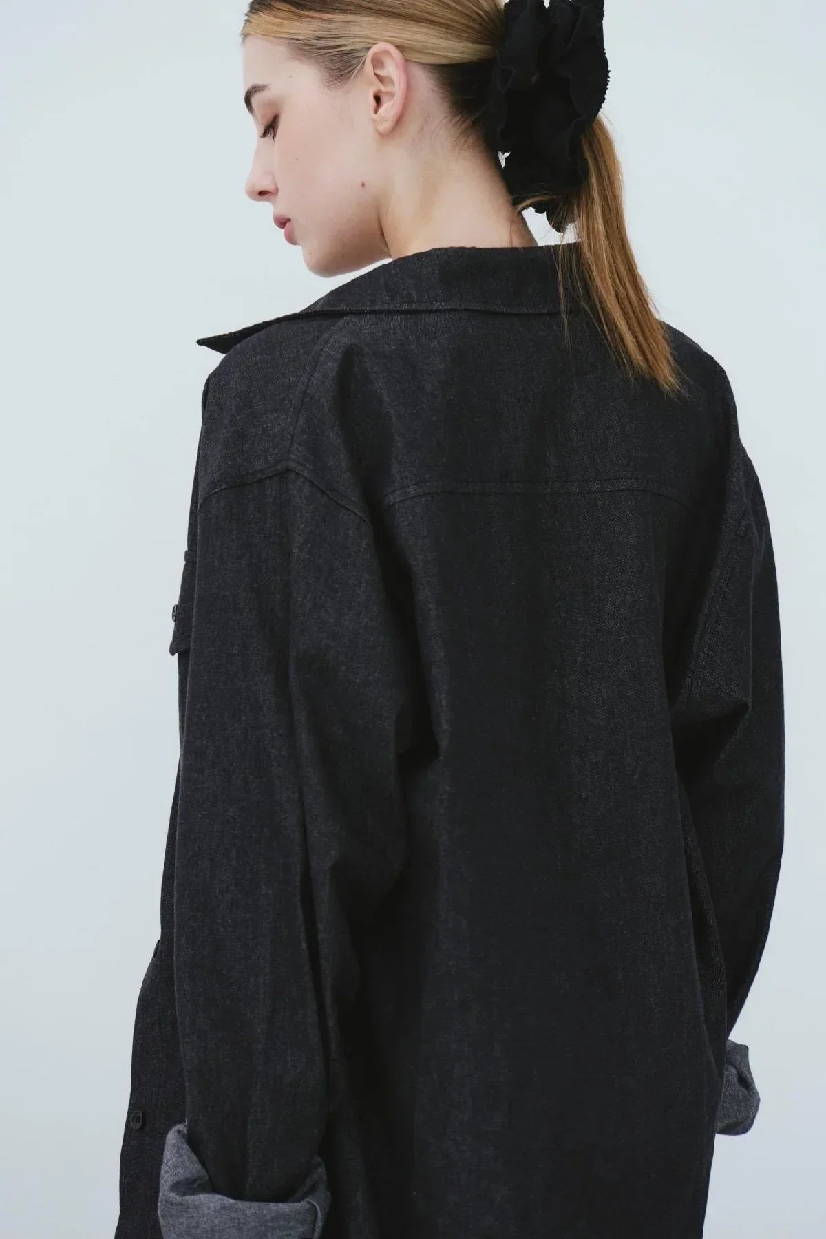 Back view of woman wearing black denim oversized shirt with rolled sleeves and black scrunchie