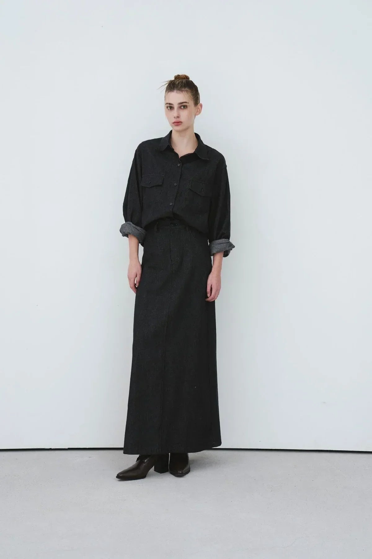 Woman wearing a black oversized button-up denim shirt with rolled sleeves and a matching black denim maxi skirt