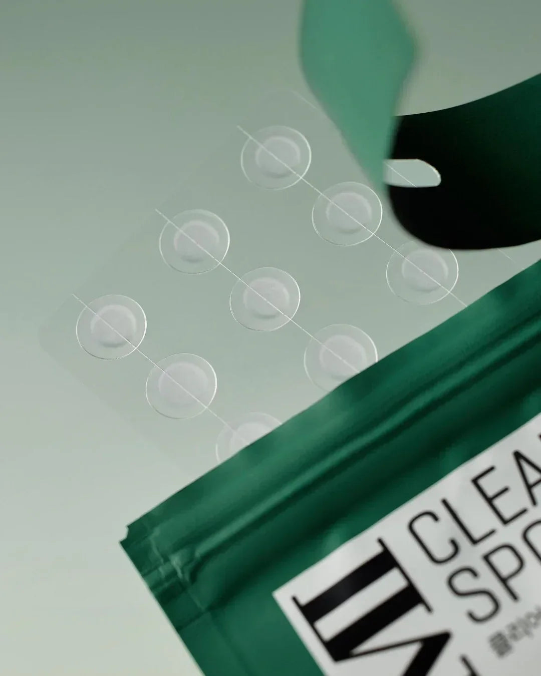 Clear spot acne patches arranged on transparent sheet with green packaging background