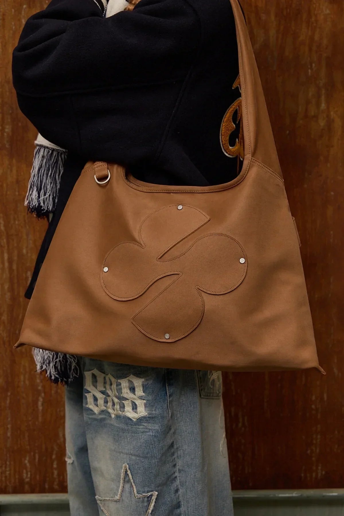 Camel artificial suede shoulder bag with clover logo worn with black jacket and denim jeans