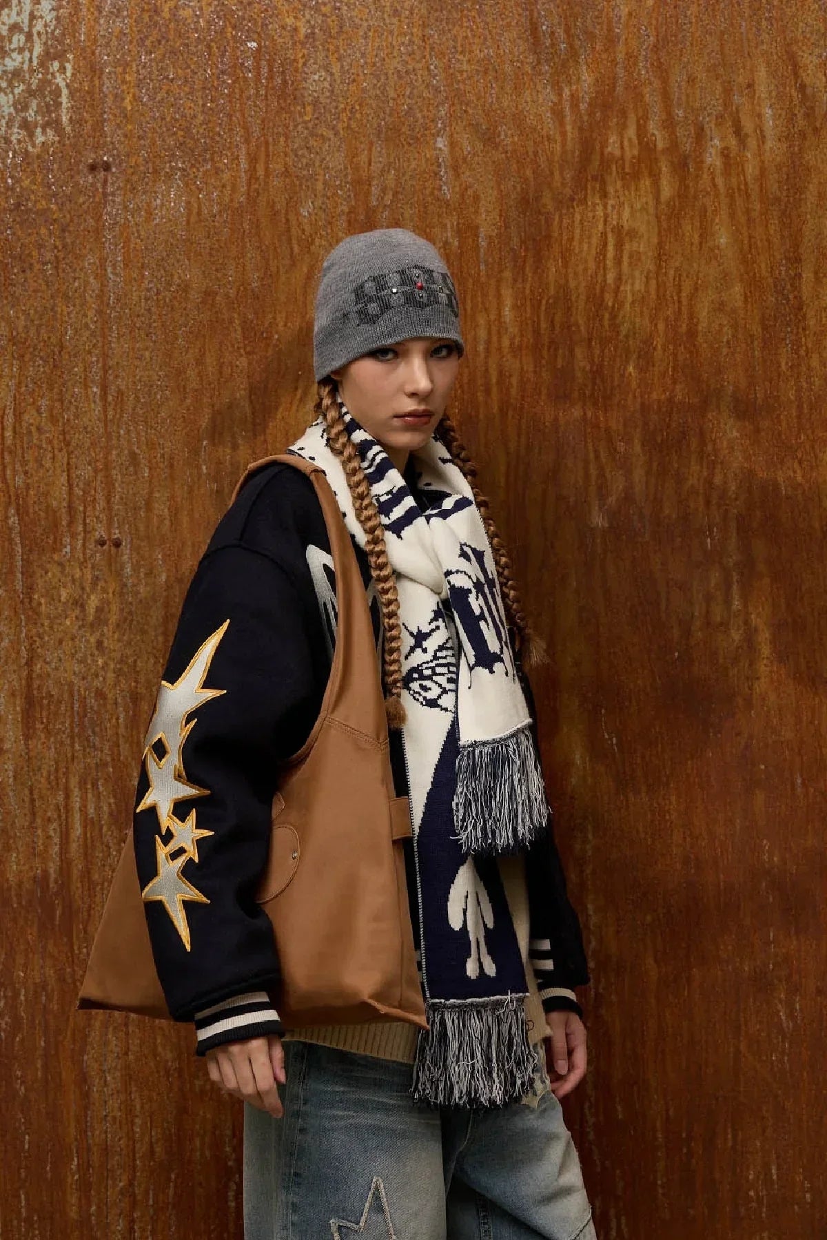 Model wearing grey beanie, star-printed black jacket, patterned scarf, camel artificial suede shoulder bag, and jeans
