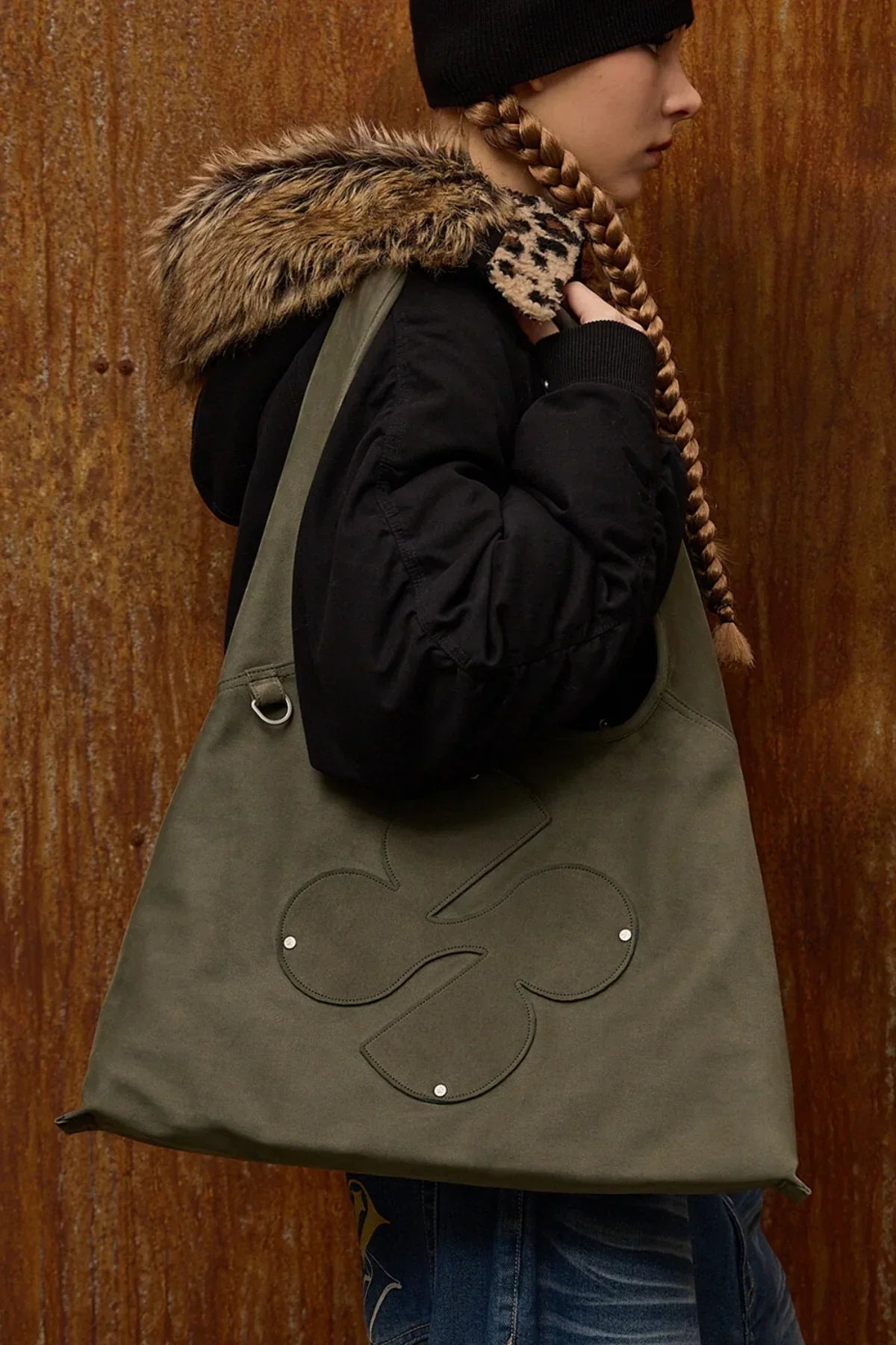 Woman wearing black jacket with fur hood carrying khaki artificial suede shoulder bag with clover logo