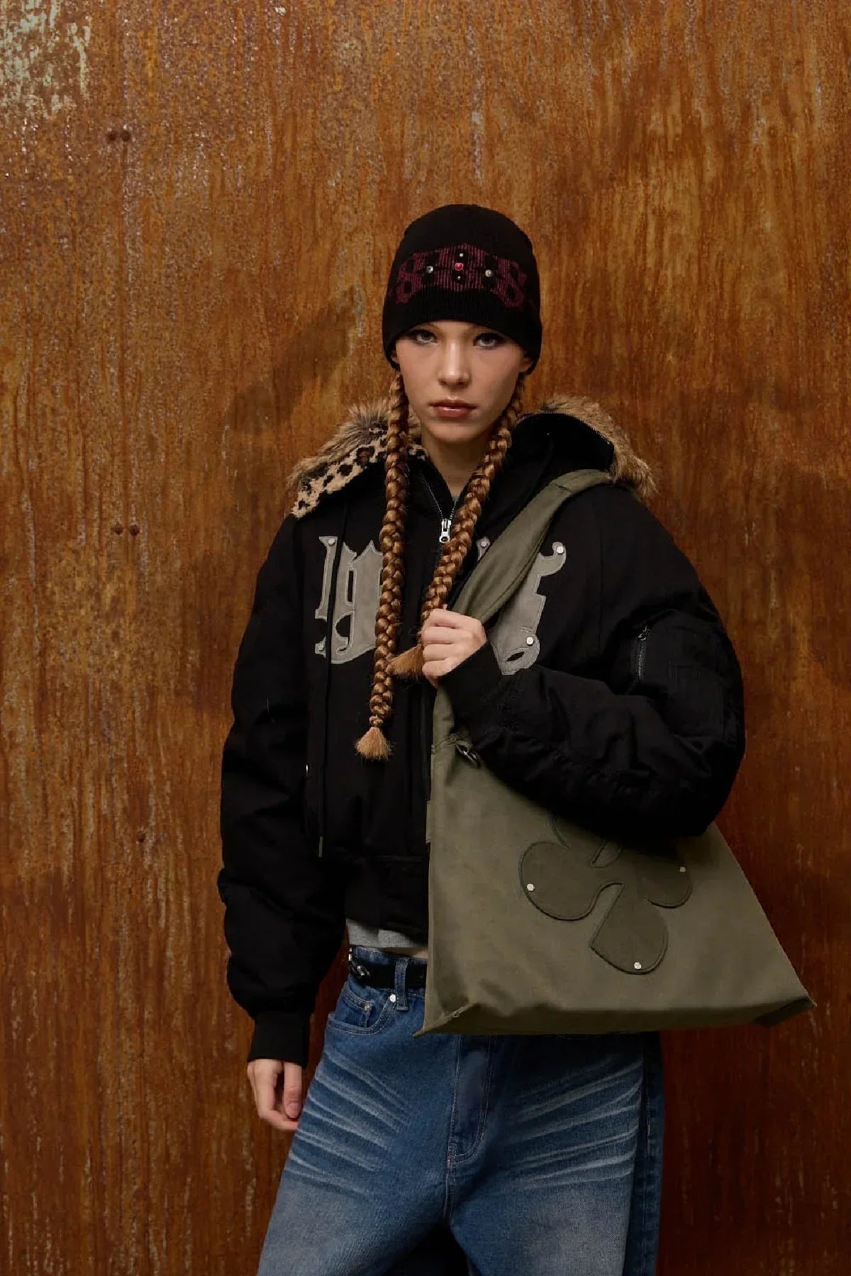Model wearing black jacket and beanie holding khaki artificial suede shoulder bag with clover logo