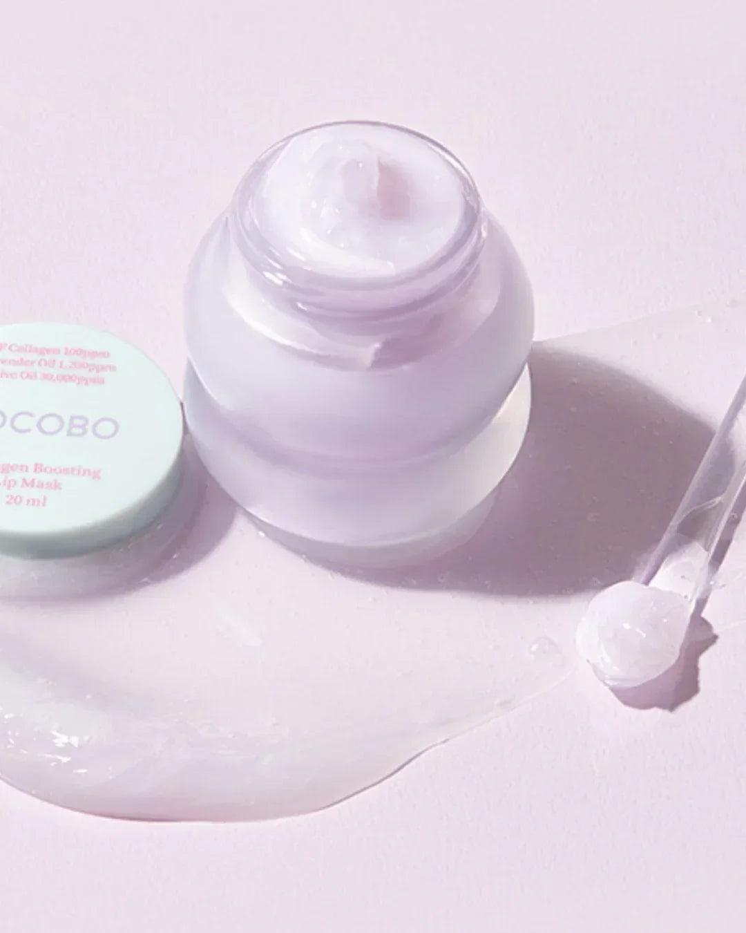 Open jar of collagen boosting lip mask with creamy texture, applied on light pink surface with dropper