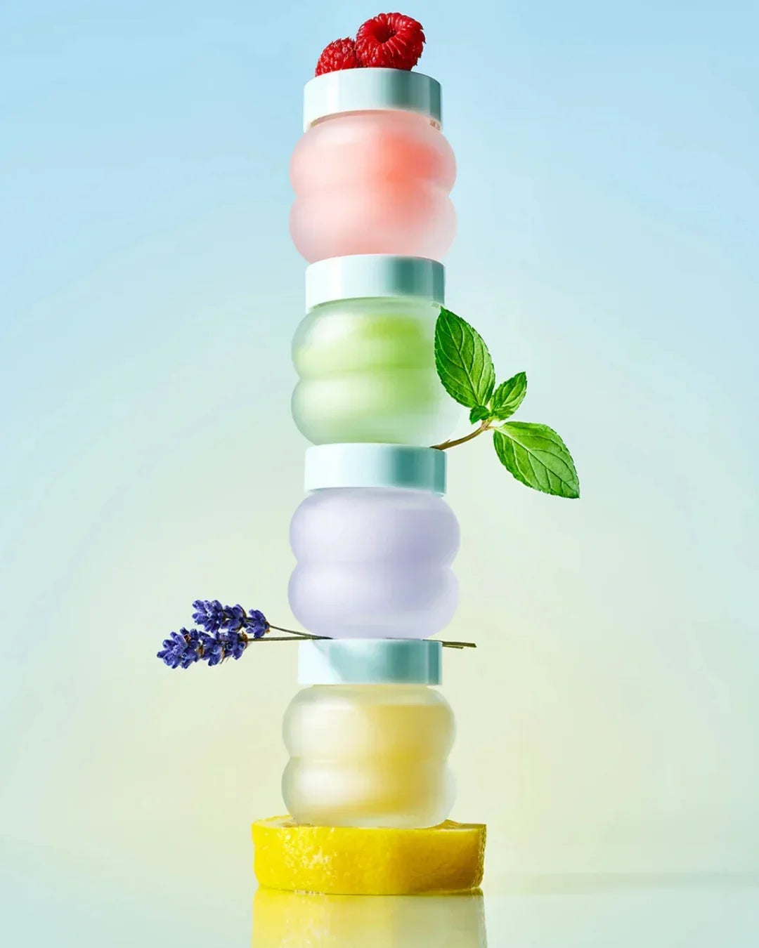 Stacked colorful skincare jars with fresh raspberry, mint, lavender, and lemon slice on pastel background