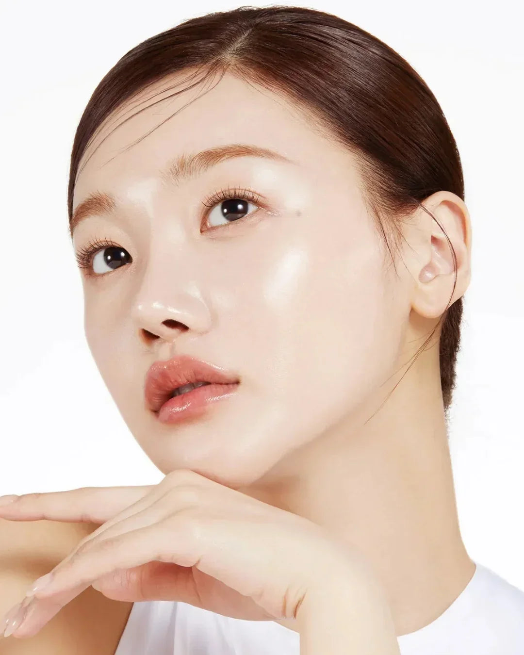 Close-up of a young woman with glowing, clear skin posing against a white background