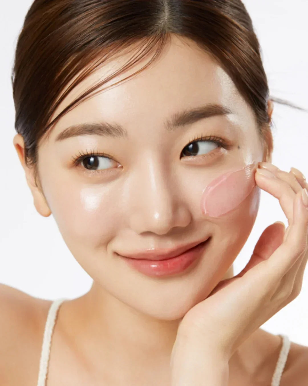 Young woman applying pink collagen jelly cream on her cheek with smooth glowing skin
