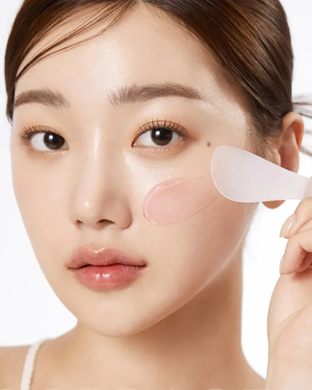 Close-up of woman applying transparent collagen jelly cream on cheek with spatula, glowing skin