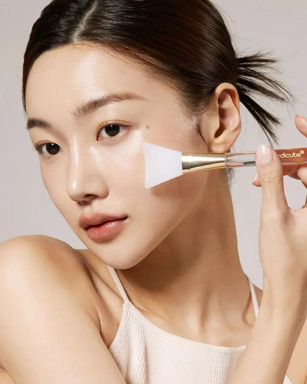 Close-up of woman applying skincare mask with silicone brush on glowing clear skin