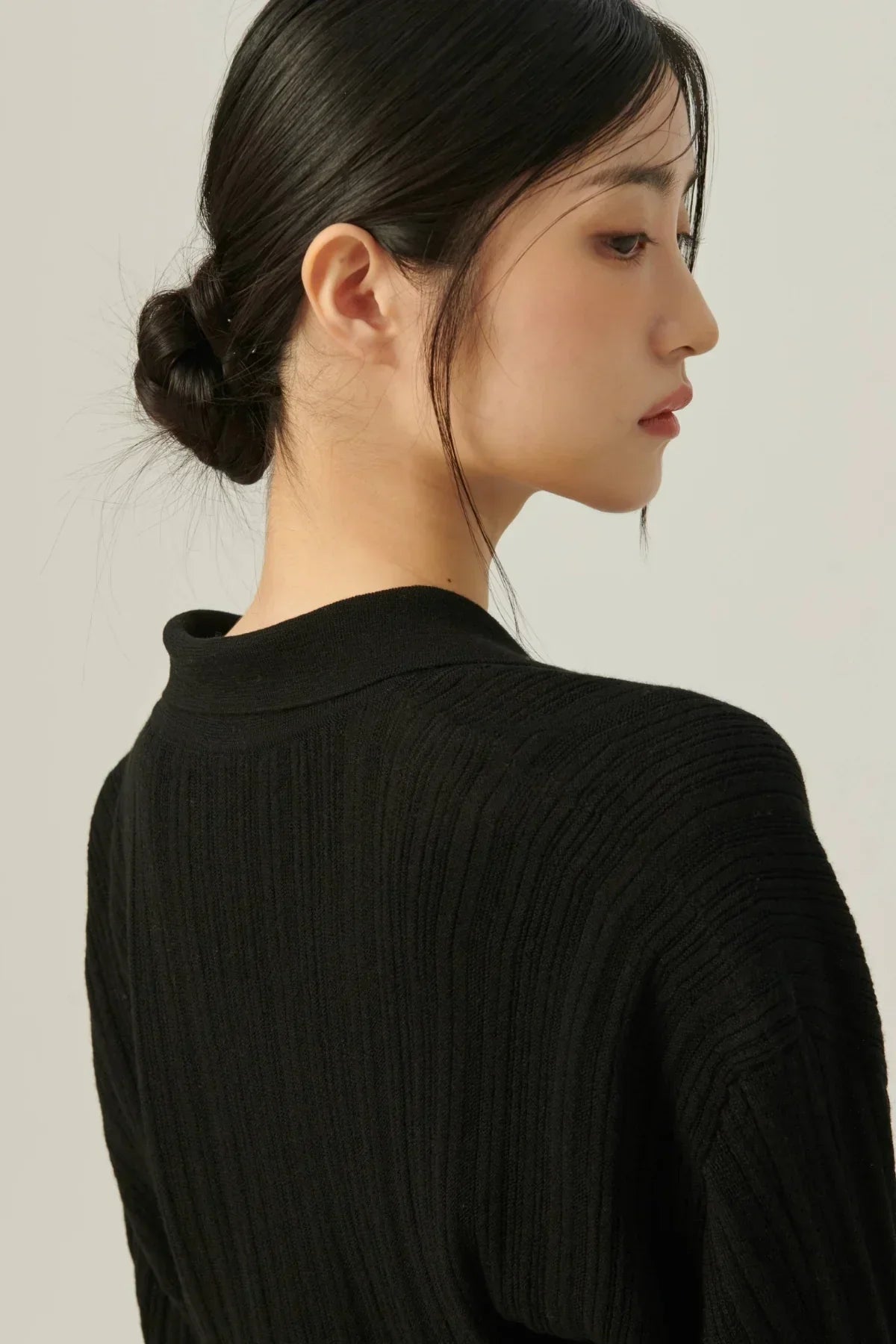 Close-up of woman with black hair bun wearing a black collared rib knit cardigan on beige background