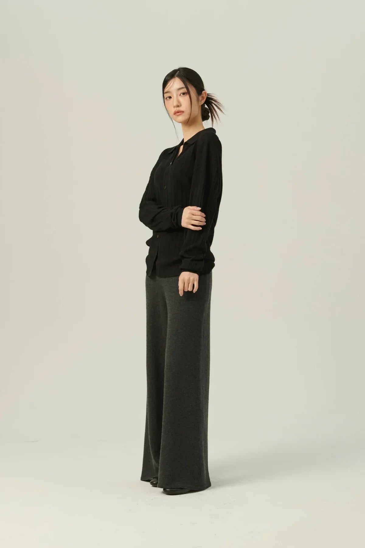 Model wearing black rib-knit collared cardigan and wide-leg dark gray pants on plain background